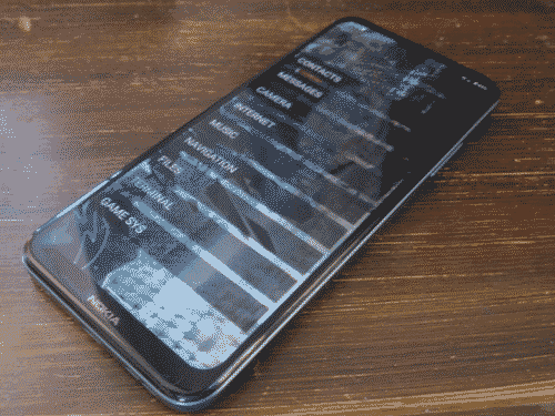 Nokia C300 face-up on a dark wooden surface. The screen is on and shows a minimal text launcher with vertically arranged text panels of white on translucent black, with the central and most intricate part of tsugumiV2-1440 as the wallpaper