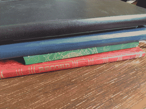 A multicolored stack of journals on a wooden desktop