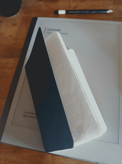a black pocket-sized dotgrid moleskinne sits atop a reMarkable 2 on a butcher-block countertop; a black pencil and the bottom of a black teacup are visible at the top of the frame