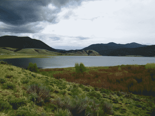 Eagle Nest Lake visible between the green hills in front and the purple mountains in back; dynamic clouds speak of rain