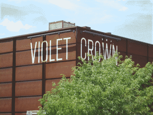 Violet Crown facade in rusty steel with a green tree in front