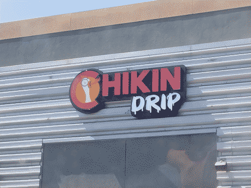 Sign for Chikin Drip, which seems like a parody of fast food; a cartoon bug-eyed chicken head holds its mouth open, breathing fire, next to the words Chikin Drip on an industrial-finish kind of modern fast food building