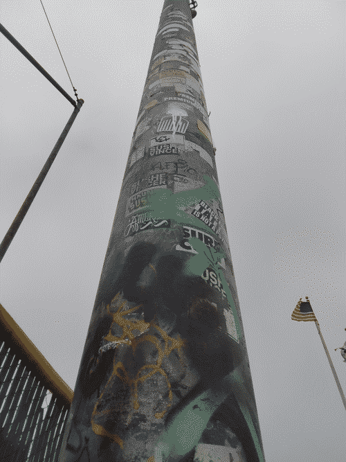 Huge light pole in the Monterey Skate Park which lights the baseball field adjacent, from the base looking up; It is covered in graffiti and stickers