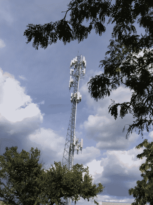 Massive radio antenna framed by coniferous trees against a dynamic sky threatening a downpour