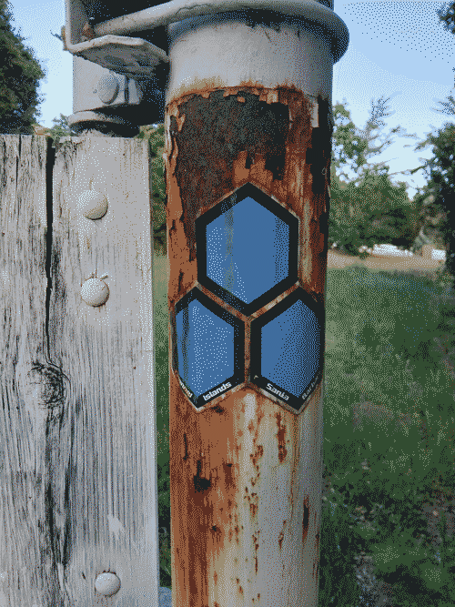 Post of a ranch gate with specks of rust and blue hexagonal stickers on it