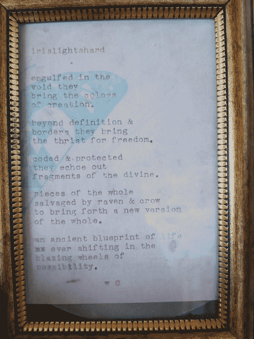 A poem printed on fancy paper with a typewriter in a gold frame, entitled _irislightshard_. It reads: engulfed in the/ void they/ bring the colors/ of creation./ beyond definition &/ borders they bring/ the thrist for freedom./ coded & protected/ the echoe out/ fragments of the divine./ pieces of the whole/ salvaged by raven & crow/ to bring forth a new version/ of teh whole./ an ancient blueprint of life/ ever shifting in the/ blazing wheels of/ possibility. -WC (Will Curious)