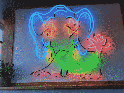 A colorful neon sign in a restaurant of an elphant head with a flower on its trunk. Underneath it are the neon letters _call me sometime_