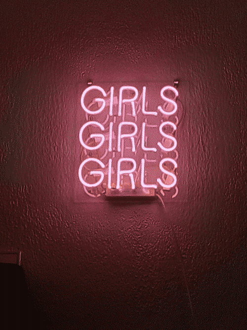 magenta neon lettering says GIRLS GIRLS GIRLS against a smoothed stucco wall