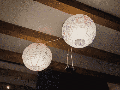 two paper lanterns gently illuminate medium-toned wood rafters against a white popcorn cieling