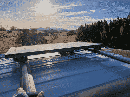 The panel clamped to the vehicle; the mounting feet and the perforated steel rails clamp onto the luggage rack on the roof of the vehicle from the top and bottom respectively