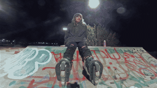 Iris sitting on a quarterpipe covered in grafitti, wearing a black jacket and torn black jeans with rollerblade Blank Sean Keane pro skates with blue laces, metal frames, and hilo wheels with larger black wheels on the outside and smaller off-white wheels on the inside.